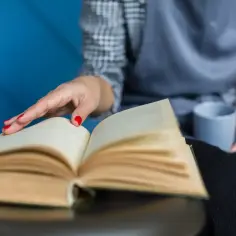 Dłoń z czerwonymi paznokciami dotyka otwartej książki.