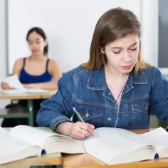 Uczennica w technikum skupiona na nauce, jak działa warunek. Obok niej koleżanka z zeszytem.