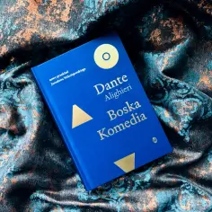 Niebieska okładka "Boskiej Komedii" Dantego Alighieri, w nowym przekładzie, leży na bogato zdobionej tkaninie. To dzieło to prawdziwa epoka w literaturze.